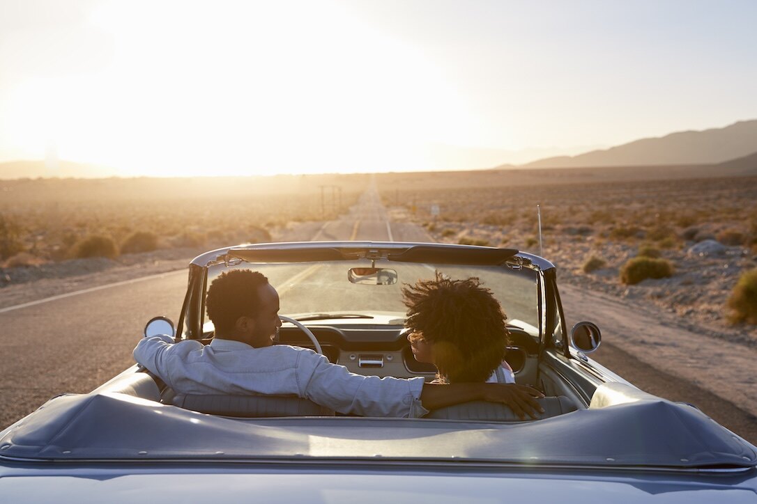 A couple driving a car on a sunny day.